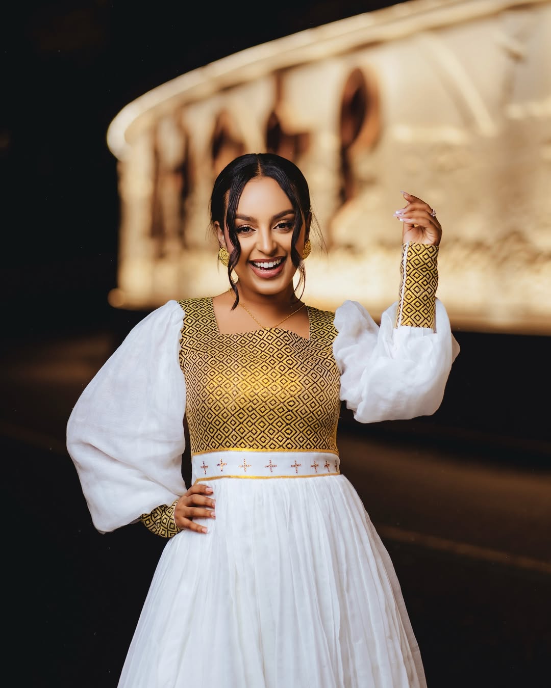 Woman wearing a gold and white traditional outfit with a blurred background. Gold Zuria Habesha Kemis New Elegant Modern Ethiopian Dress ethgebya gebeya habesha kemis