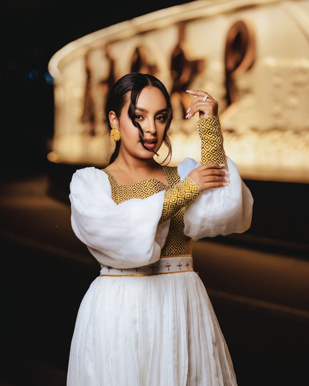 Woman in a traditional outfit with white and gold elements, posing in front of a decorative background.Gold Zuria Habesha Kemis New Elegant Modern Ethiopian Dress ethgebya gebeya habesha kemis