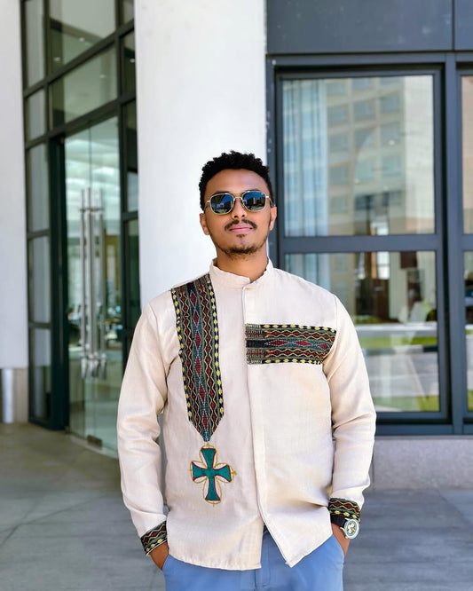 Man wearing a traditional outfit with intricate patterns in an urban setting. Cream Luxury Habesha Men’s Shirt New Modern Ethiopian Style ethgebya gebeya wen wond habehsa