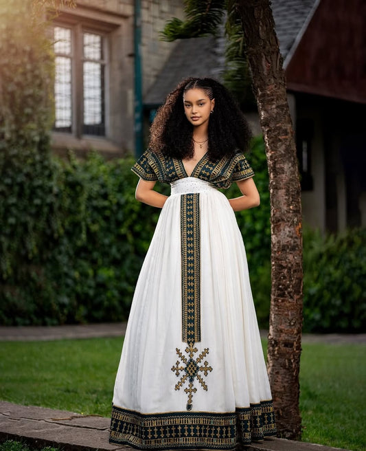 Woman in a white dress with black and gold embroidery standing outdoors. Golden & Green Modern Habesha Kemis Elegant Ethiopian ethgebya gebeyaDress