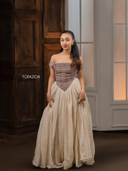Woman wearing a patterned off-shoulder top and beige skirt with 'Topazion' branding. Modern Brown & Beige Habesha Kemis ethgebya
