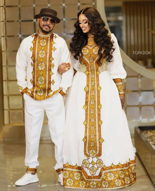 Man and woman in matching traditional outfits with gold embroidery in a decorative setting. Golden Ethiopian Habesha Couple Outfit | New Matching Modern Set