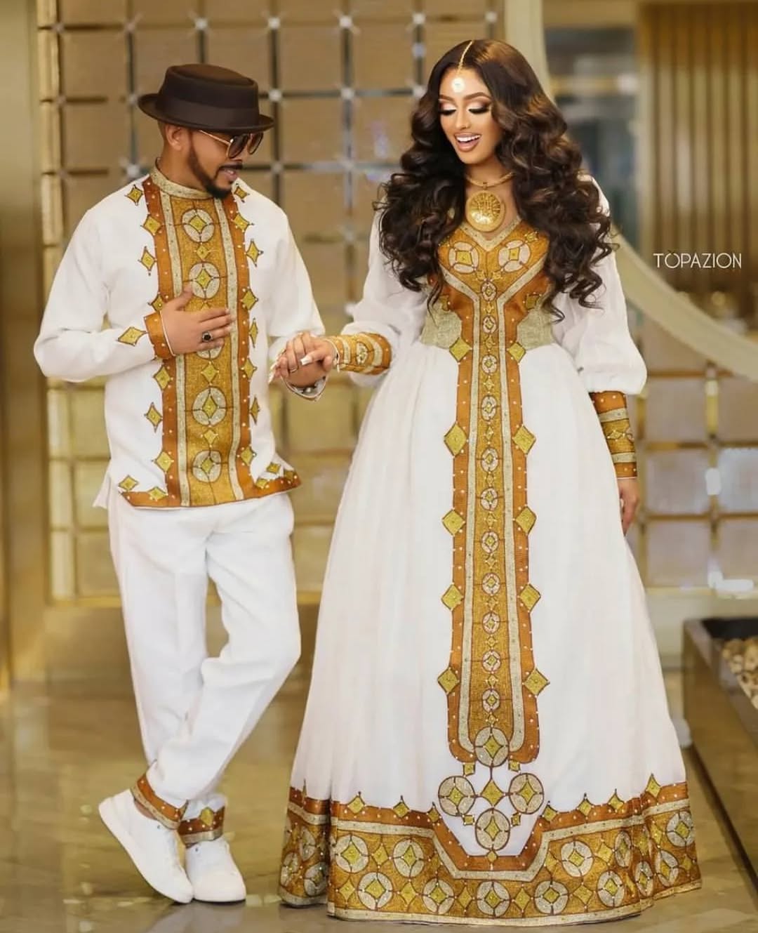 Man and woman in traditional white and gold outfits walking together  Golden Ethiopian Habesha Couple Outfit | New Matching Modern Setindoors.