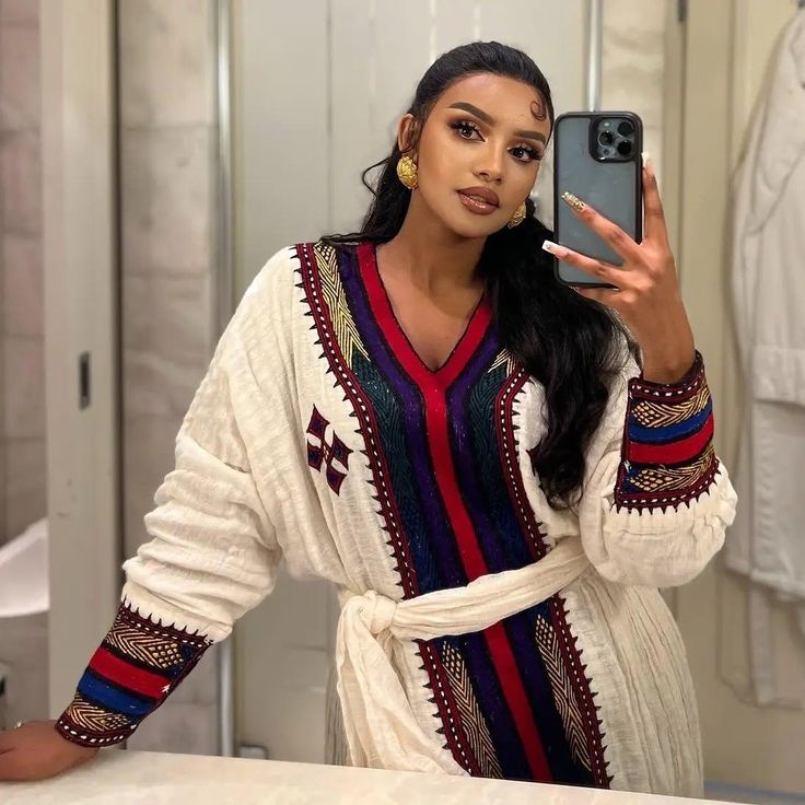 Woman taking a mirror selfie wearing a colorful dress with intricate  Elegant Ethiopian & Eritrean Axum Habesha Dress Ethgebyapatterns.