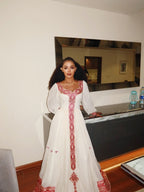 Woman in a white dress with red embroidery standing in front of a mirror. New Pink Zuria Habesha Kemis Handcrafted Ethiopian Traditional Dress Ethiopia Gebebya Ethgebya