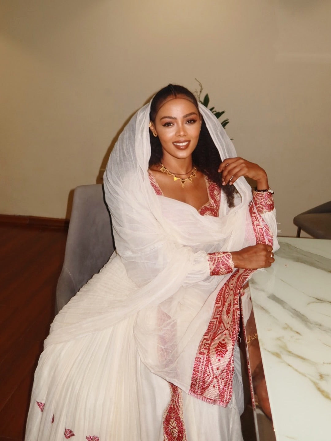 Woman wearing a white saree with red patterns, sitting indoors. New Pink Zuria Habesha Kemis Handcrafted Ethiopian Traditional Dress Ethiopia Gebebya Ethgebya