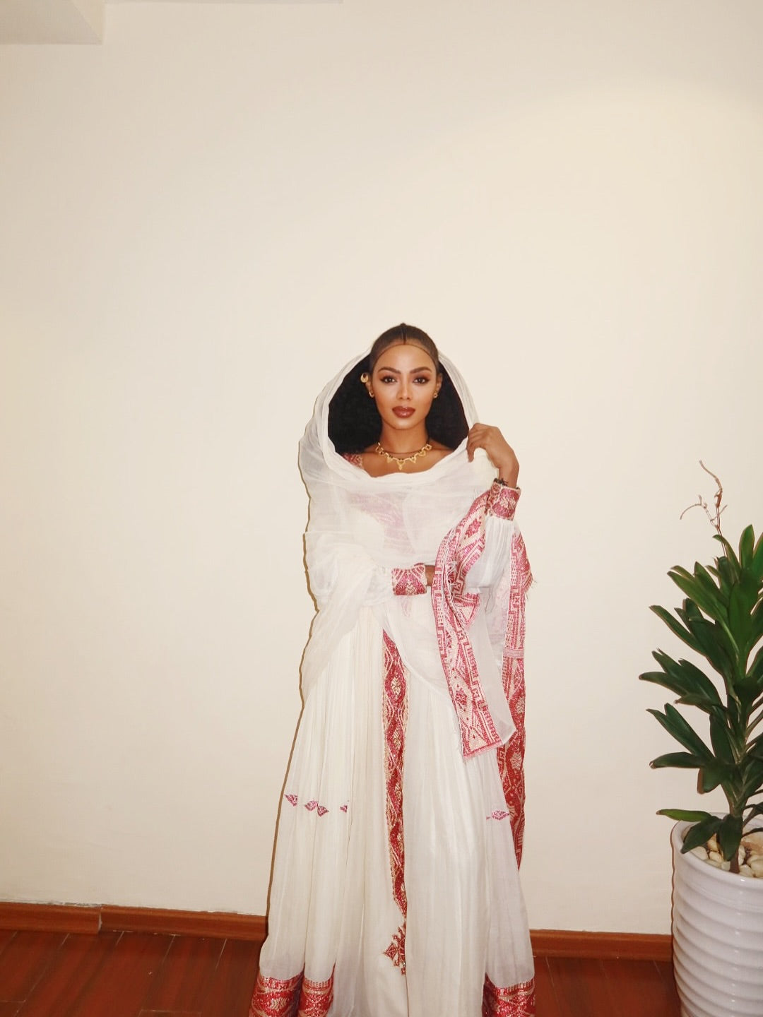 Woman wearing a white and red embroidered traditional outfit with a plant in the background. New Pink Zuria Habesha Kemis Handcrafted Ethiopian Traditional Dress Ethiopia Gebebya Ethgebya
