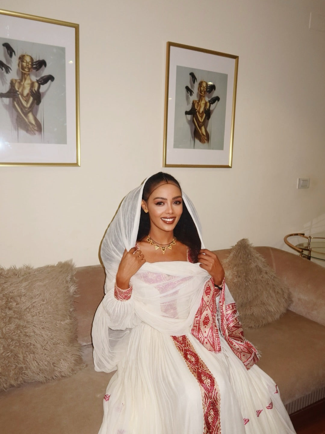 Woman in a white and red embroidered dress standing in a living room with framed artwork on the wall. New Pink Zuria Habesha Kemis Handcrafted Ethiopian Traditional Dress Ethiopia Gebebya Ethgebya