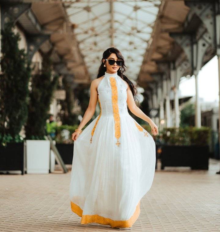 Woman in a white dress with yellow accents walking outdoors. Yellow Modern Zuria Habesha Kemis Handcrafted Ethiopian Dress ethgebya gebeya usa habesha kemis