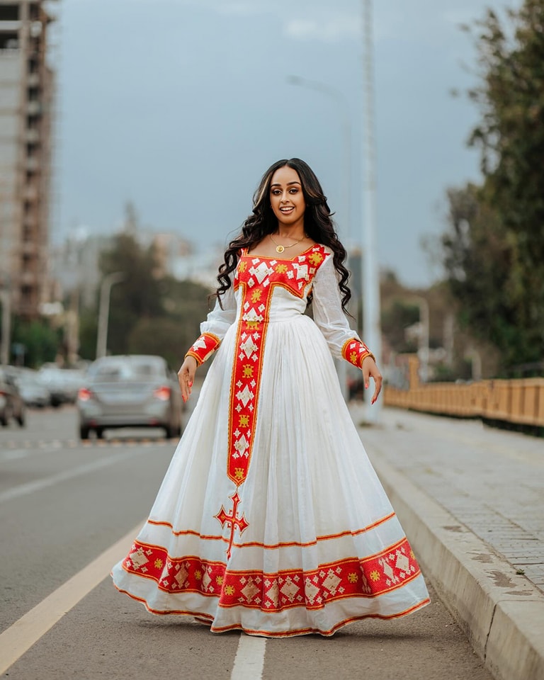 Woman in a white and red traditional dress standing on a street. Red Zuria Habesha Kemis New Modern Ethiopian Dress ethgebya gebeya usa habesha kemis