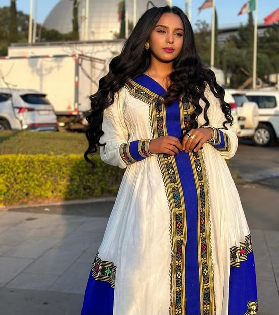 Woman in a traditional outfit with blue and white design outdoors. Elegant Handmade Habesha Kemis | Ethiopian Traditional Dress for Women ethgebya gebeya usa