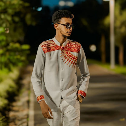 Man wearing a traditional outfit with red patterns on a blurred outdoor background. Handwoven Red Habesha Men’s Shirt Ethiopian Traditional Outfit ethgebya ethiopian gebeya