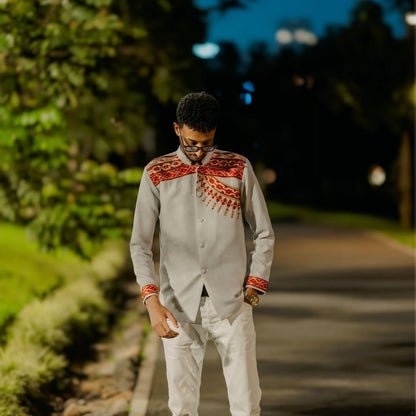 Man wearing a traditional outfit with intricate patterns walking on a path surrounded by greenery. Handwoven Red Habesha Men’s Shirt Ethiopian Traditional Outfit ethgebya ethiopian gebeya