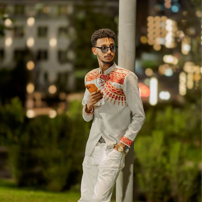 Man in a stylish outfit with a patterned shirt and sunglasses, holding a phone, against a blurred cityscape background. Handwoven Red Habesha Men’s Shirt Ethiopian Traditional Outfit ethgebya ethiopian gebeya