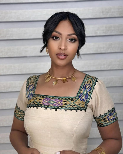 Woman wearing a traditional outfit with intricate embroidery against a neutral background New Beige Zuria Habesha Kemis Modern Handcrafted Ethiopian Dress ethgebya gebeya