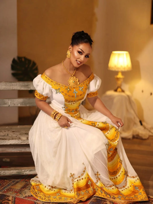 Woman in a traditional yellow and white outfit sitting indoors. Yellow Modern Zuria Kemis Elegant Handcrafted Ethiopian Dress ethgebya gebeya