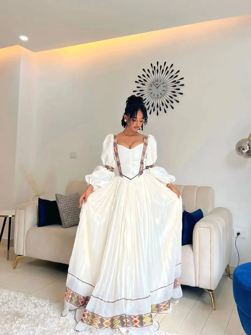 Woman in a white dress with colorful details standing in a modern living room. One of a Kind Modern Zuria Kemis | Handcrafted Ethiopian Dress