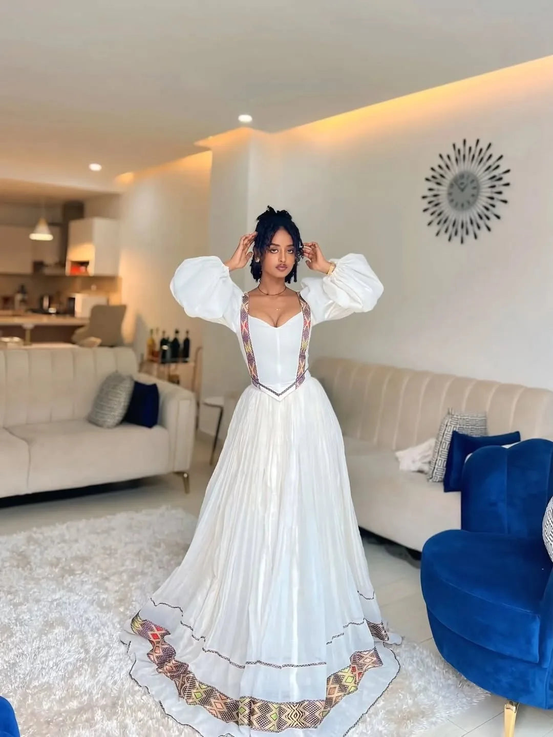 Woman in a white dress with intricate designs standing in a modern living room. One of a Kind Modern Zuria Kemis | Handcrafted Ethiopian Dress