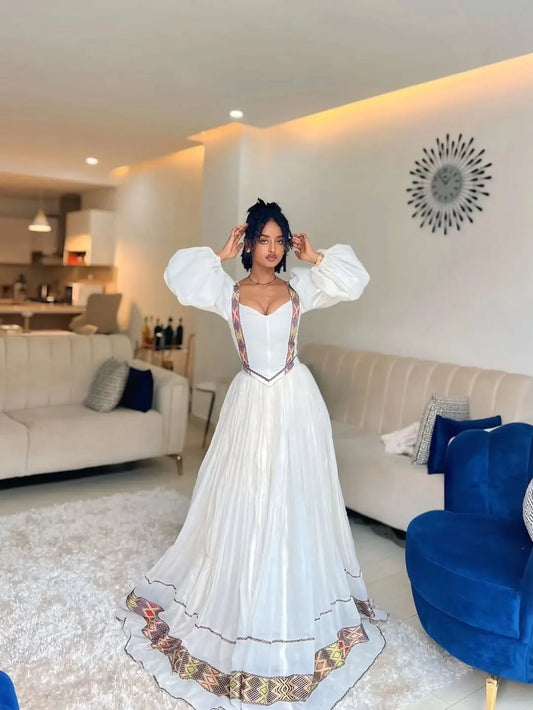 Woman in a white dress with intricate designs standing in a modern living room. One of a Kind Modern Zuria Kemis | Handcrafted Ethiopian Dress