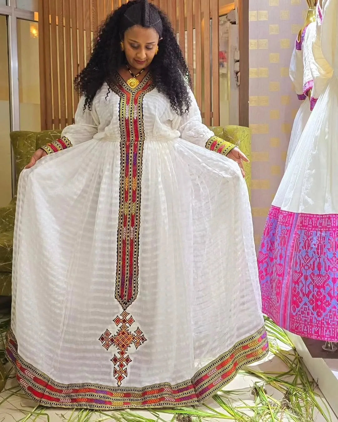 Woman wearing a white dress with colorful embroidery sitting on a couch. Elegant Zuria Habesha Kemis New Modern Ethiopian Traditional Dress ethgebya gebeya