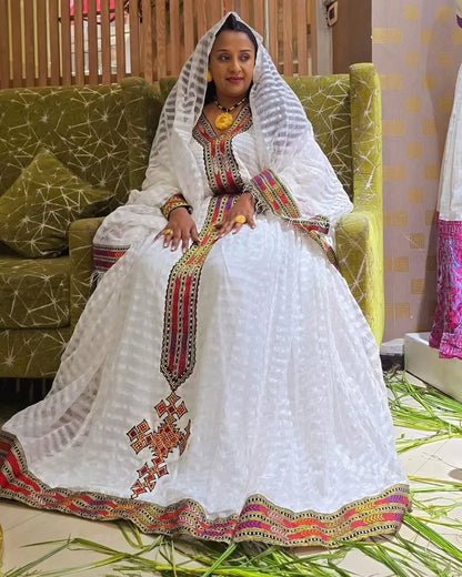 Woman in traditional embroidered outfit sitting on a green sofa. Elegant Zuria Habesha Kemis New Modern Ethiopian Traditional Dress ethgebya gebeya