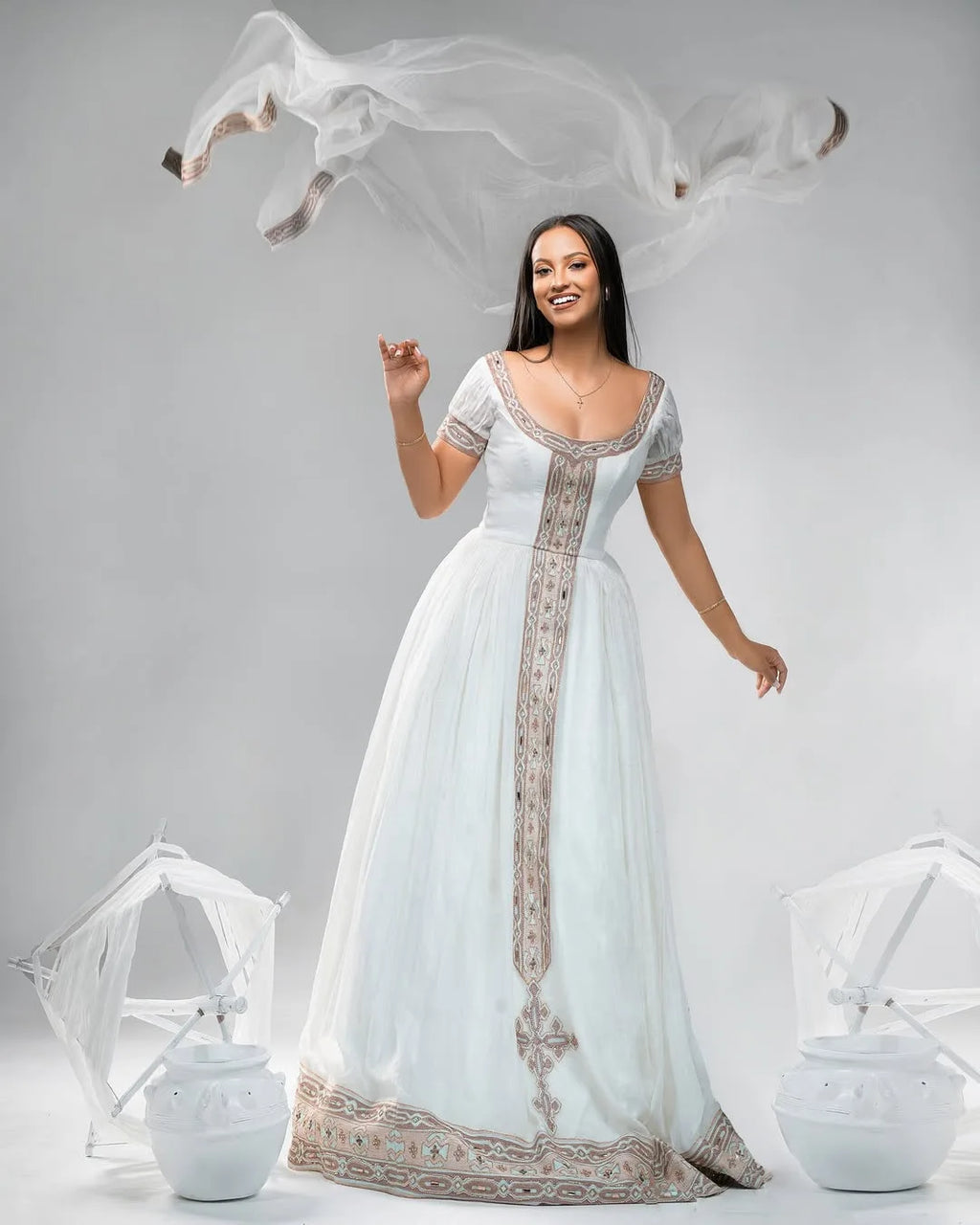 Woman in a white gown with intricate designs on a gray background