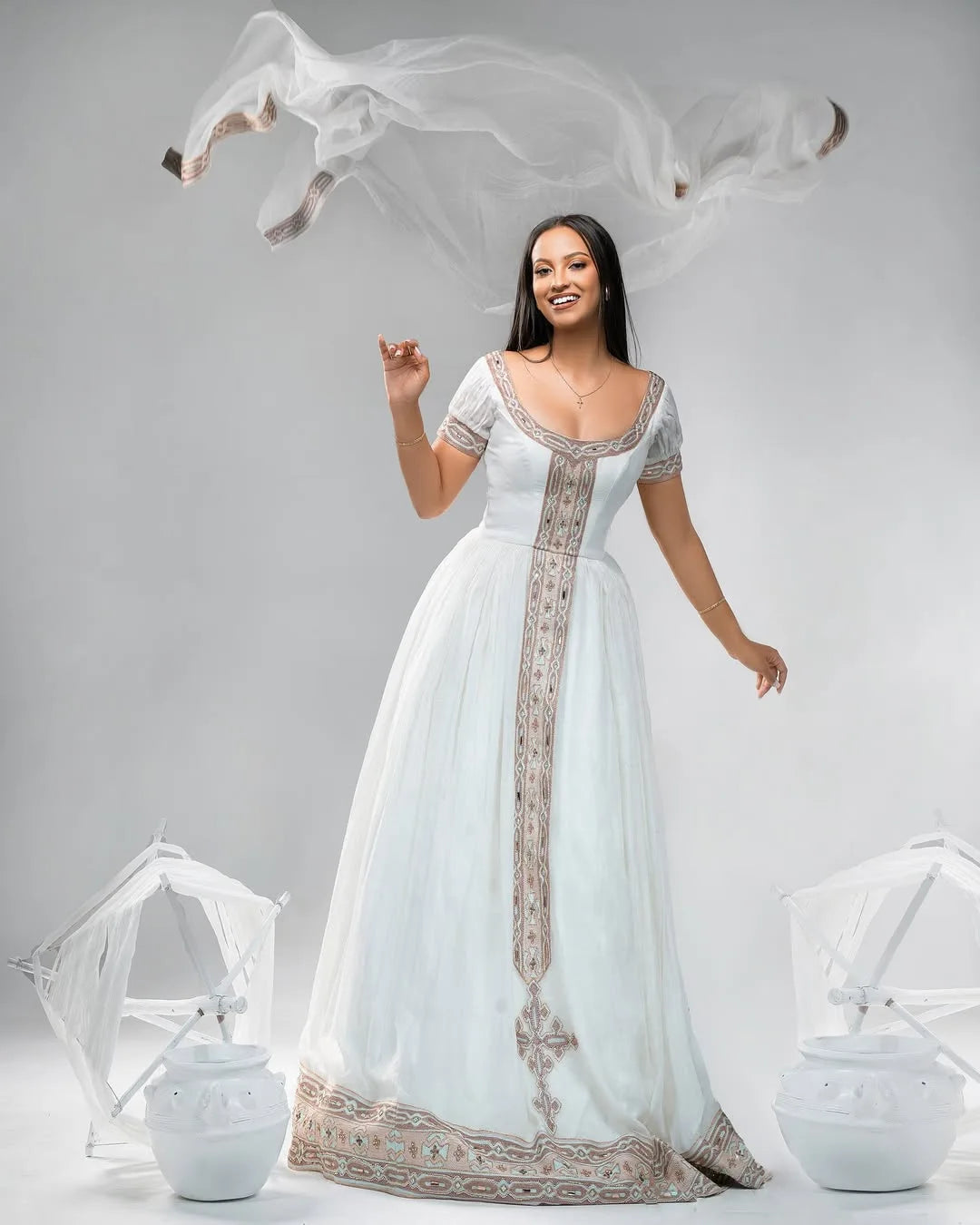 Woman in a white gown with intricate designs on a gray background