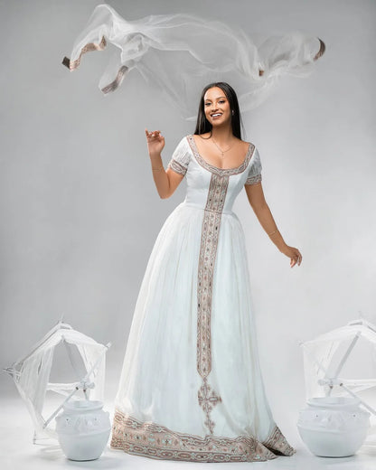 Woman in a white gown with intricate designs on a gray background