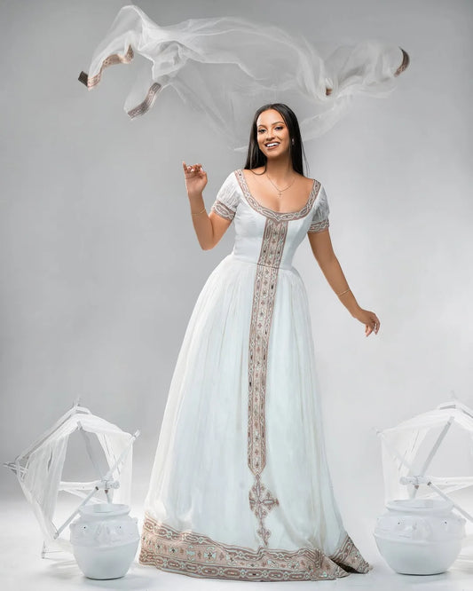 Woman in a white gown with intricate designs on a gray background