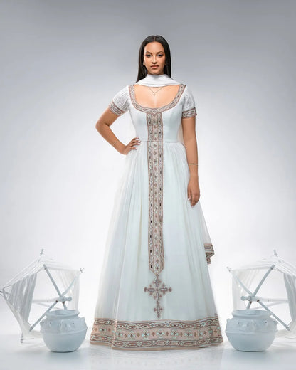 Woman wearing a white dress with intricate patterns in a minimalistic setting