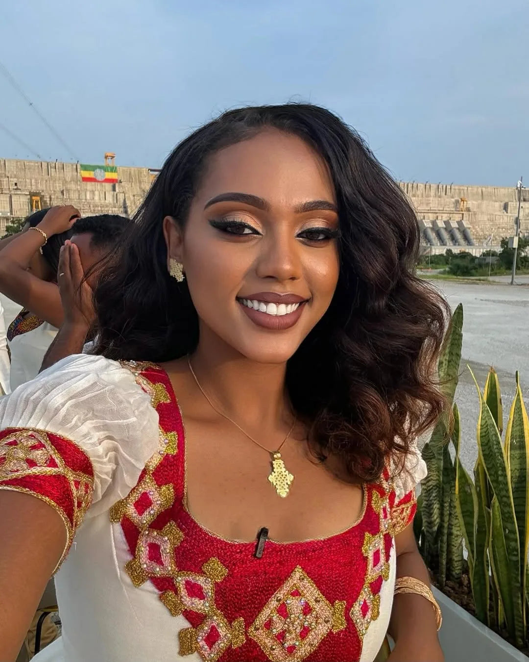 Woman in a red and gold traditional outfit with a scenic background