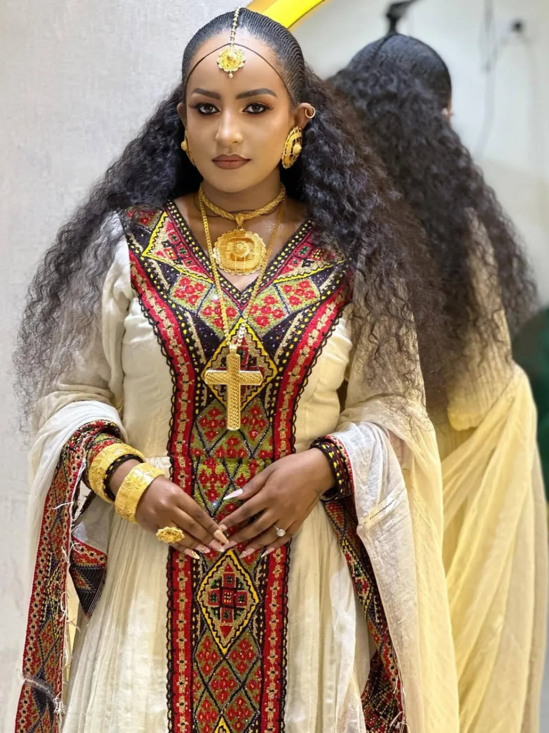 Person wearing traditional attire with intricate patterns and gold jewelry against a white background. axum habesha kemis Shop Now & Enjoy Free Worldwide Shipping – Fast Delivery to USA, Canada, UK, and Europe!