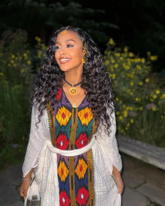 Woman wearing a colorful traditional outfit with a dark background axum habesha kemis ethgebya