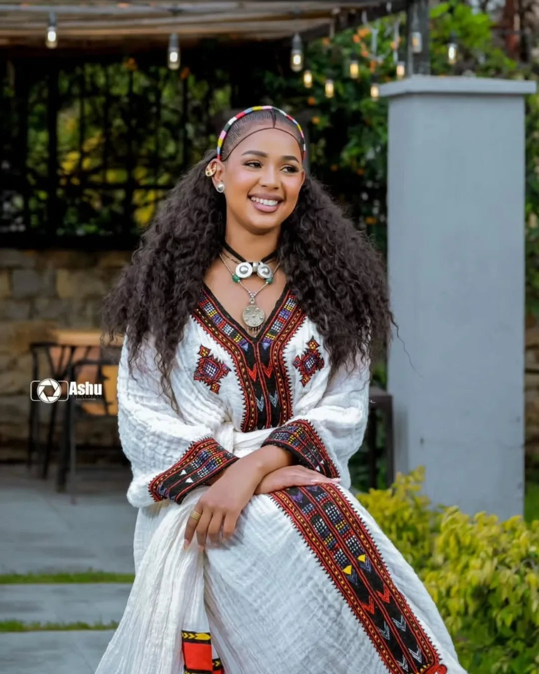 Woman in a traditional outfit with intricate patterns sitting outdoors. Elegant Axum Habesha Kemis ethgebya