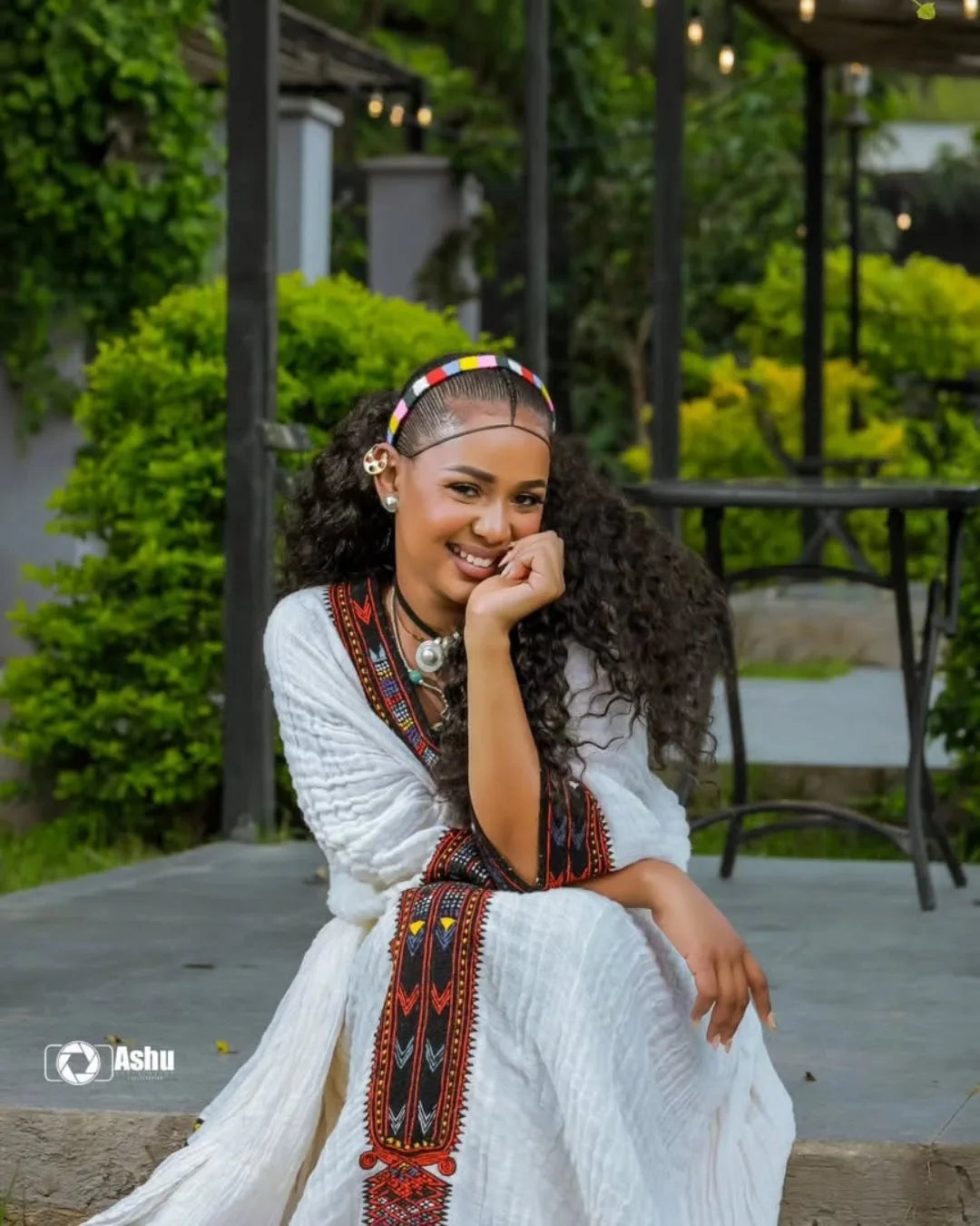 Woman in a white dress with decorative elements sitting outdoors. Elegant Axum Habesha Kemis ethgebya