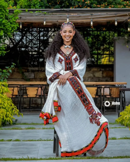 Woman in a traditional outfit with intricate patterns sitting outdoors. Elegant Axum Habesha Kemis ethgebya