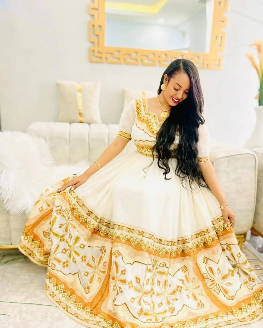 Woman in a white and gold traditional outfit sitting on a white couch. Modern Zuria Kemis ethgebya