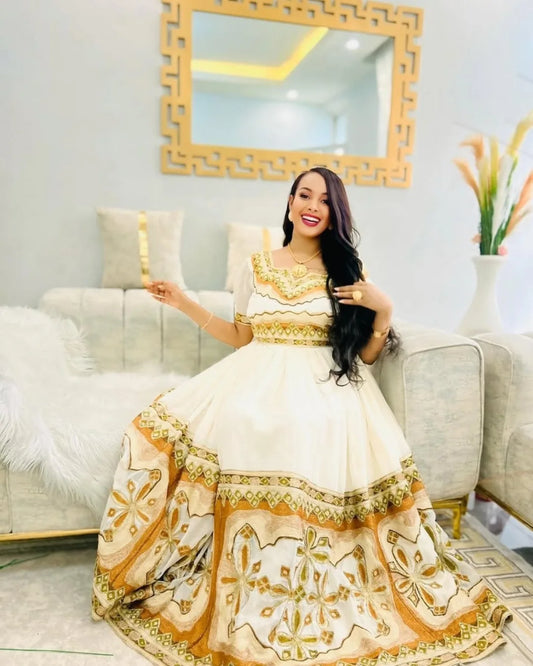 Woman in a white and gold dress sitting on a couch in a decorated room. Modern Zuria Kemis ethgebya