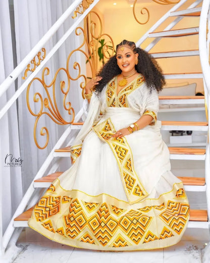 Woman in a white and gold traditional outfit sitting on a staircase. Orange & Yellow Zuria Habesha Kemis Modern Ethiopian Traditional Dress Ethgebya