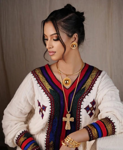 Woman wearing traditional embroidered clothing with jewelry against a neutral backgroundElegant Ethiopian & Eritrean Axum Habesha Dress Ethgebya