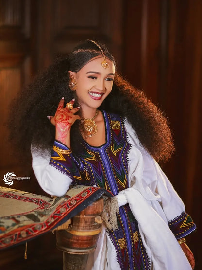 Woman in traditional attire with intricate jewelry and a decorative background. New Ethiopian & Eritrean Axum Habesha Dress Handwoven Tilet Kemis Ethiopia Gebeya Ethgebya