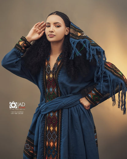 Woman wearing a traditional blue embroidered dress with a headscarf, posing against a neutral background. Dark Blue Raya Cultural Dress Handwoven Ethiopian Habesha Kemis ethgebya gebeya usa habesha kemis