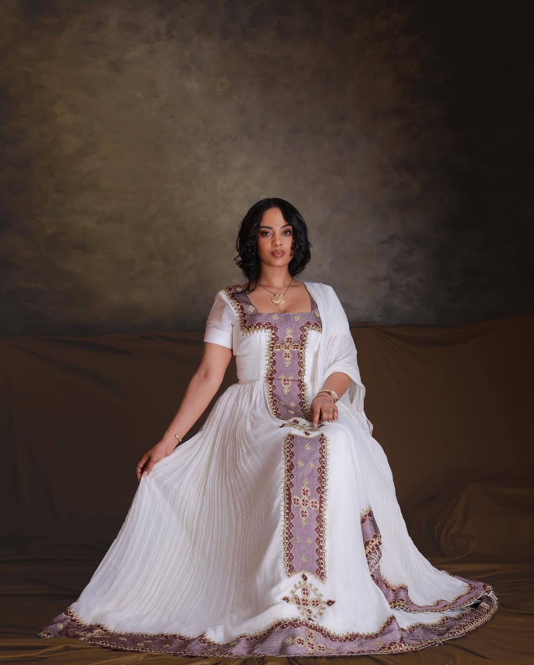 Woman in a white and purple embroidered dress against a brown background. Rose Gold Zuria Habesha Kemis Handcrafted Modern Ethiopian Dress Ethiopia Gebeya Ethgebya