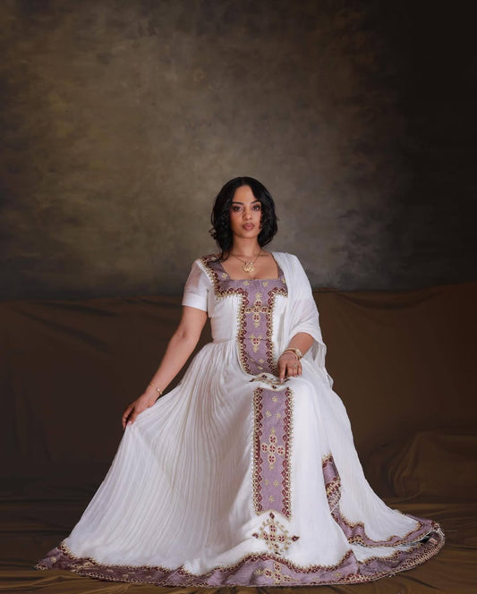 Woman in a white and purple embroidered dress against a brown background. Rose Gold Zuria Habesha Kemis Handcrafted Modern Ethiopian Dress Ethiopia Gebeya Ethgebya