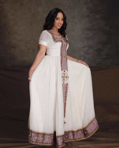 Woman wearing a white and purple traditional outfit with intricate designs on a dark background. Rose Gold Zuria Habesha Kemis Handcrafted Modern Ethiopian Dress Ethiopia Gebeya Ethgebya