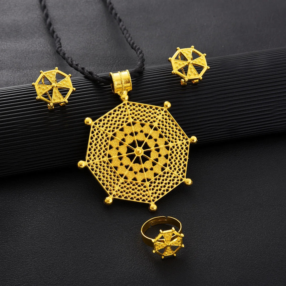 Gold geometric necklace, earrings, and ring on a black background