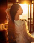 Woman in a white dress standing in a warm, sunlit room. Orange & Golden Zuria Kemis | Modern Handcrafted Ethiopian Dress