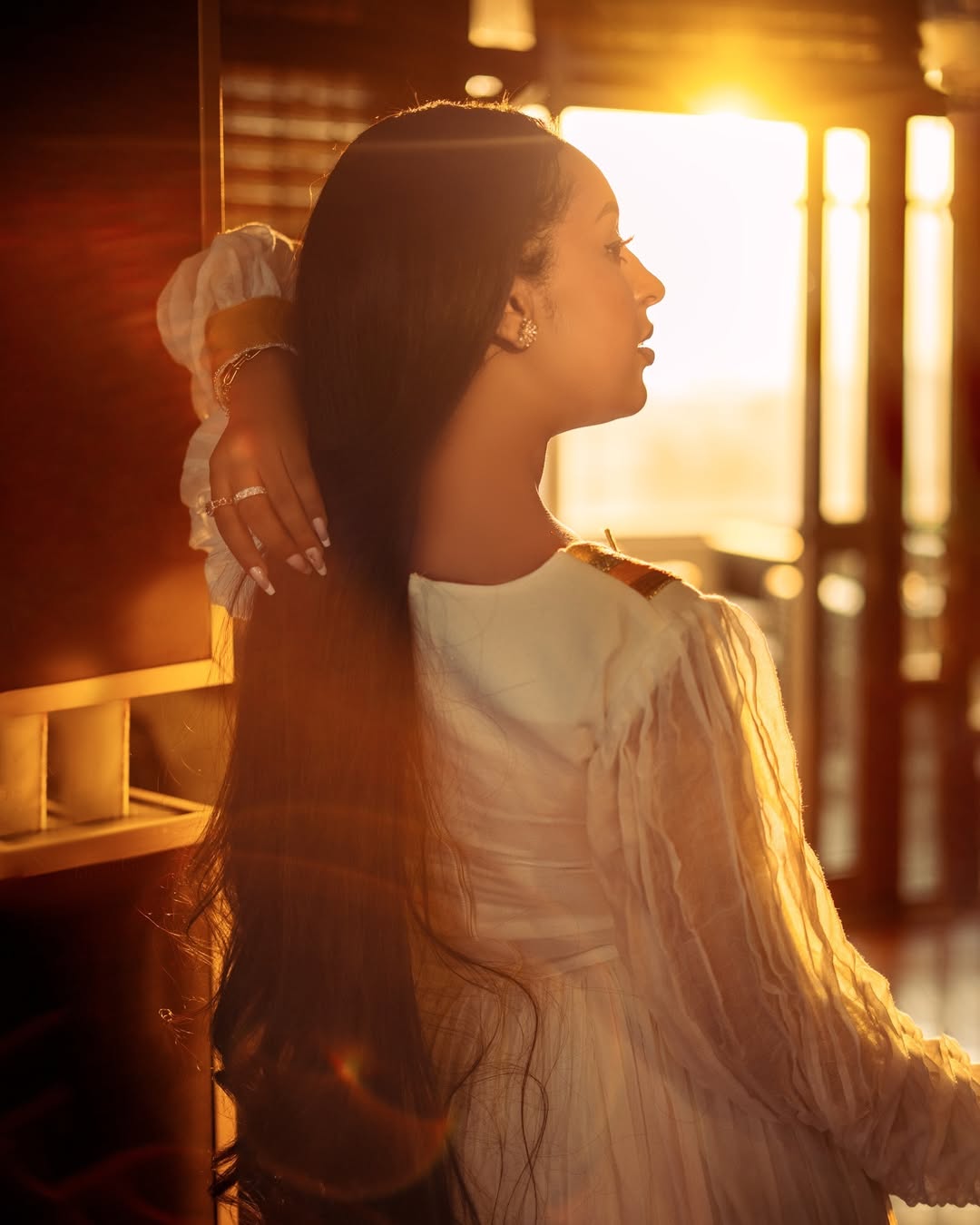Woman in a white dress standing in a warm, sunlit room. Orange & Golden Zuria Kemis | Modern Handcrafted Ethiopian Dress