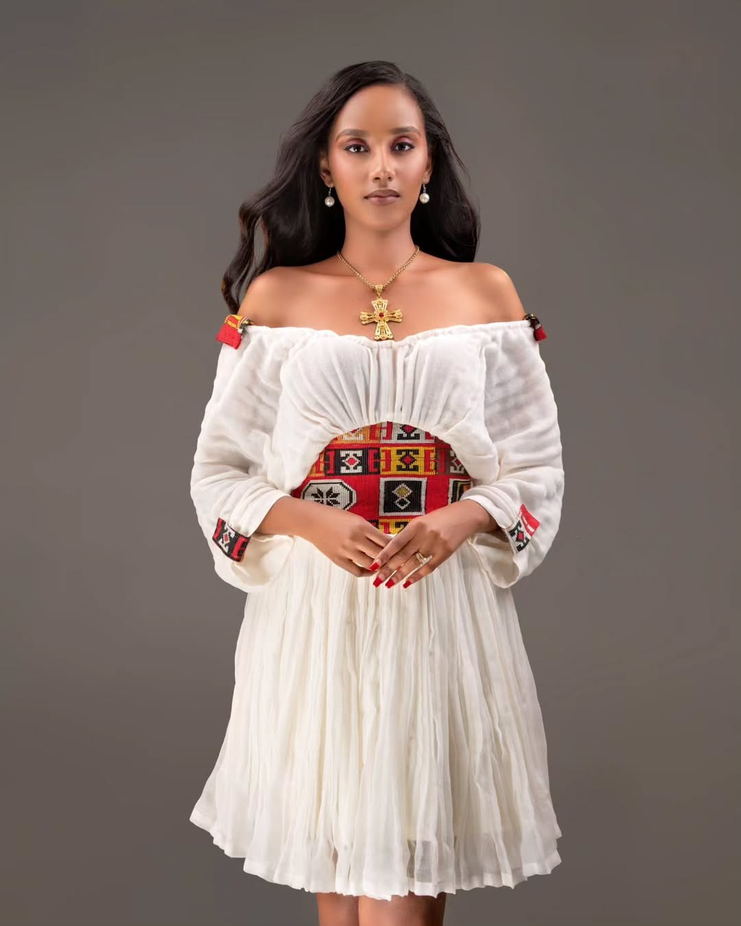 Woman wearing a white off-shoulder dress with colorful patterns on a gray background Red Tilet Habesha Short Kemis New Modern Ethiopian Dress ethgebya gebeya