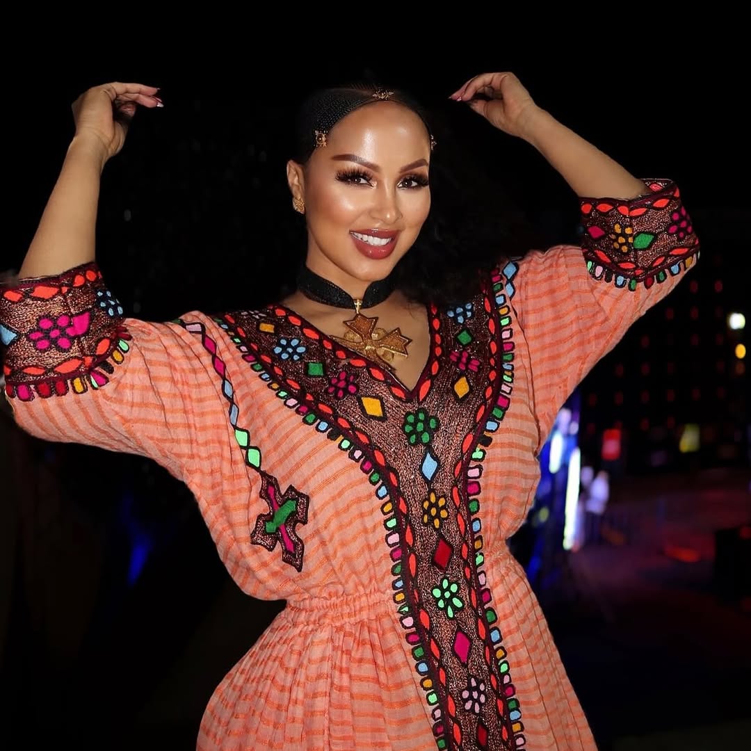 Woman wearing a colorful embroidered dress with a blurred Gold Sand Ethiopian & Eritrean Axum Habesha Dress Ethgebya